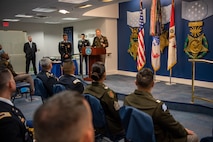 a man stands behind a podium and talks to a group of people in the audience.