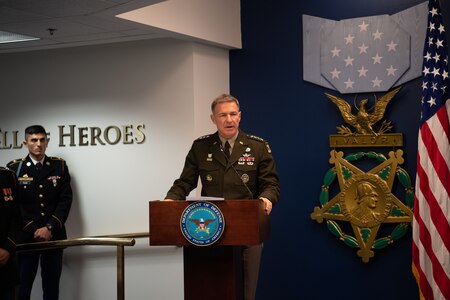 Man stands behind a podium on a stage wearing an army uniform.