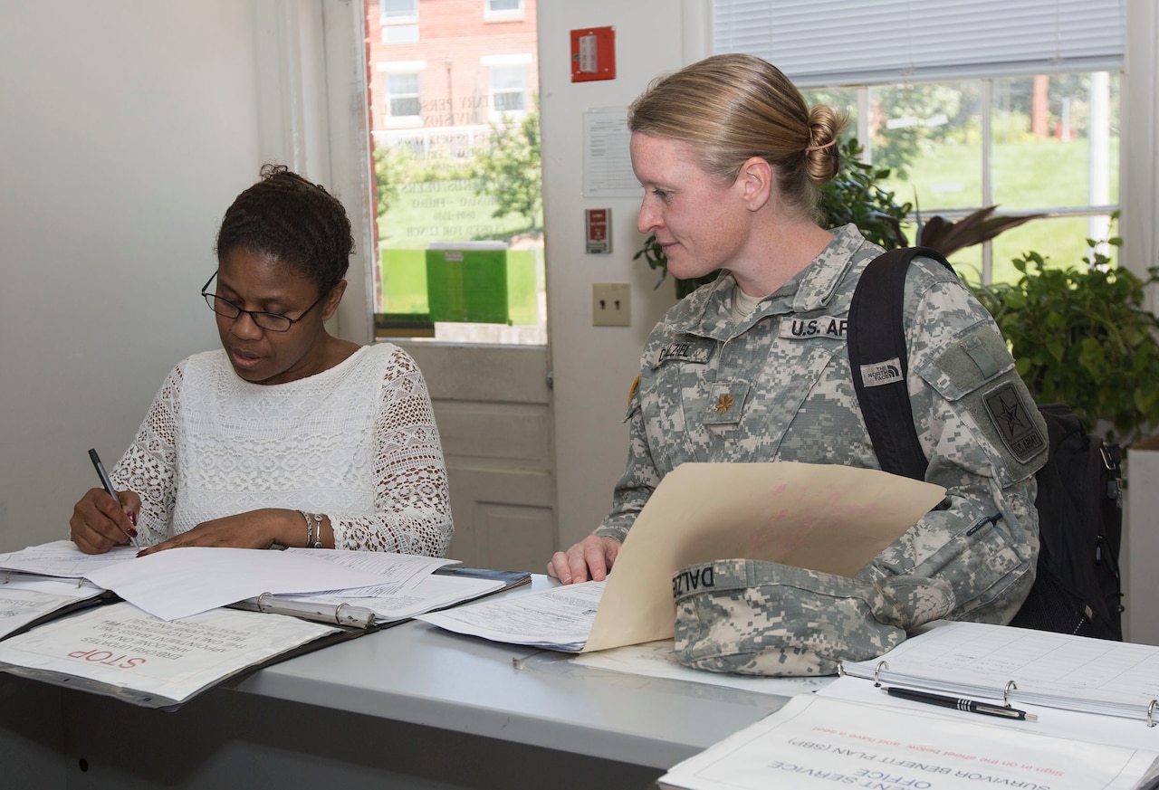 A woman assists a soldier with paper work.