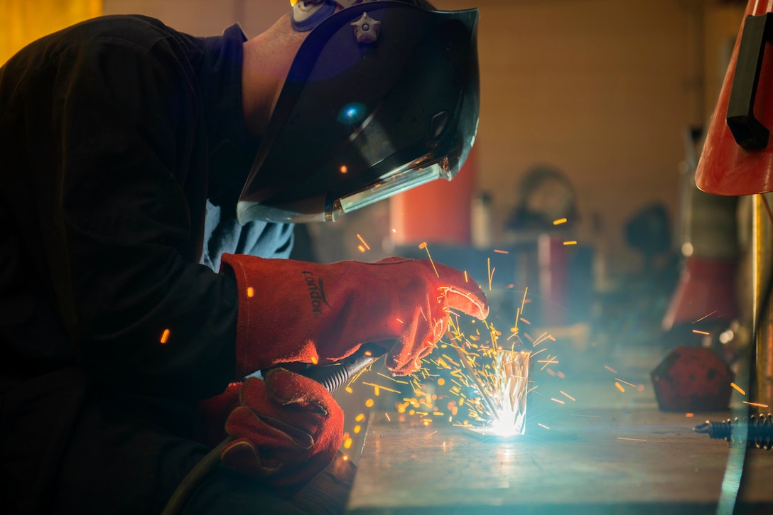 An airman welds a piece of metal as sparks fly.