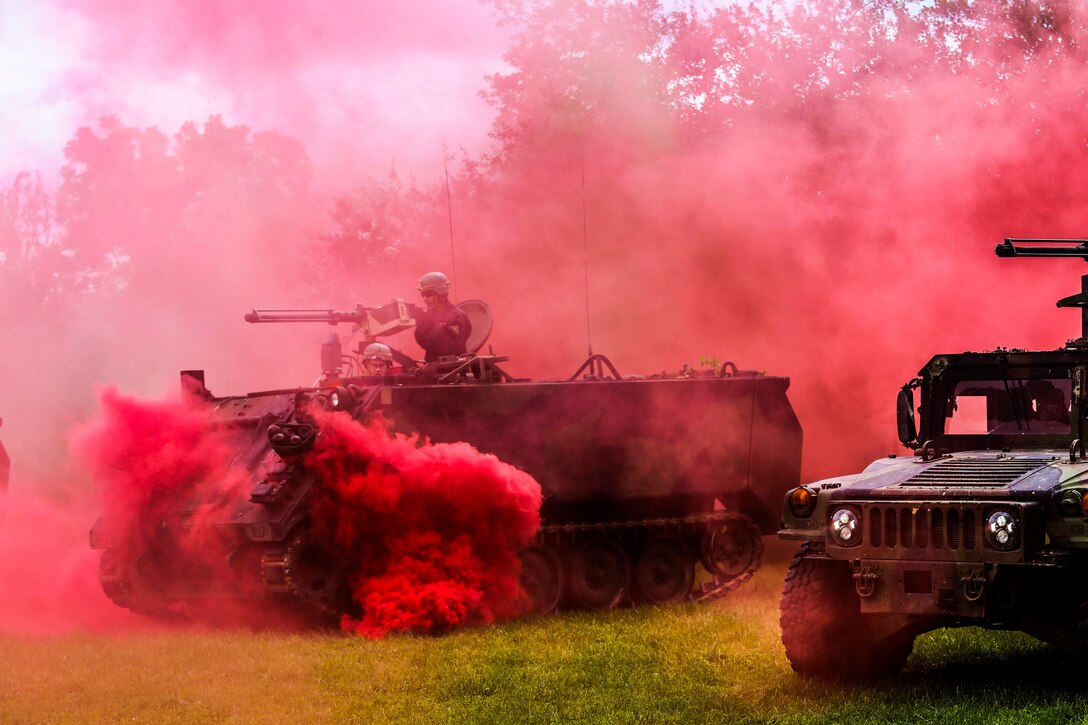 A soldier aims a weapon from a tank surrounded by clouds of a pink smoke.