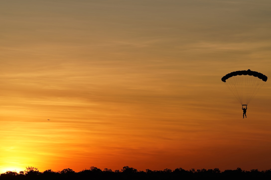 A service member freefalls with a parachute under a sunlit sky.