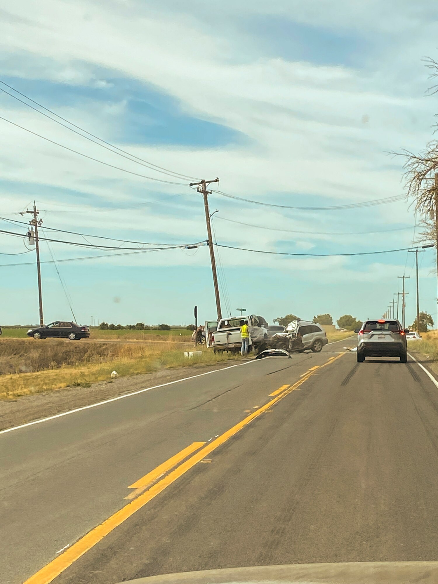 A long road leads to a car crash scene.