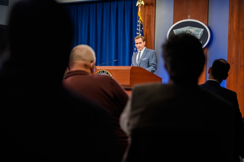 A man stands behind a lectern. In front of him are a group of seated individuals.