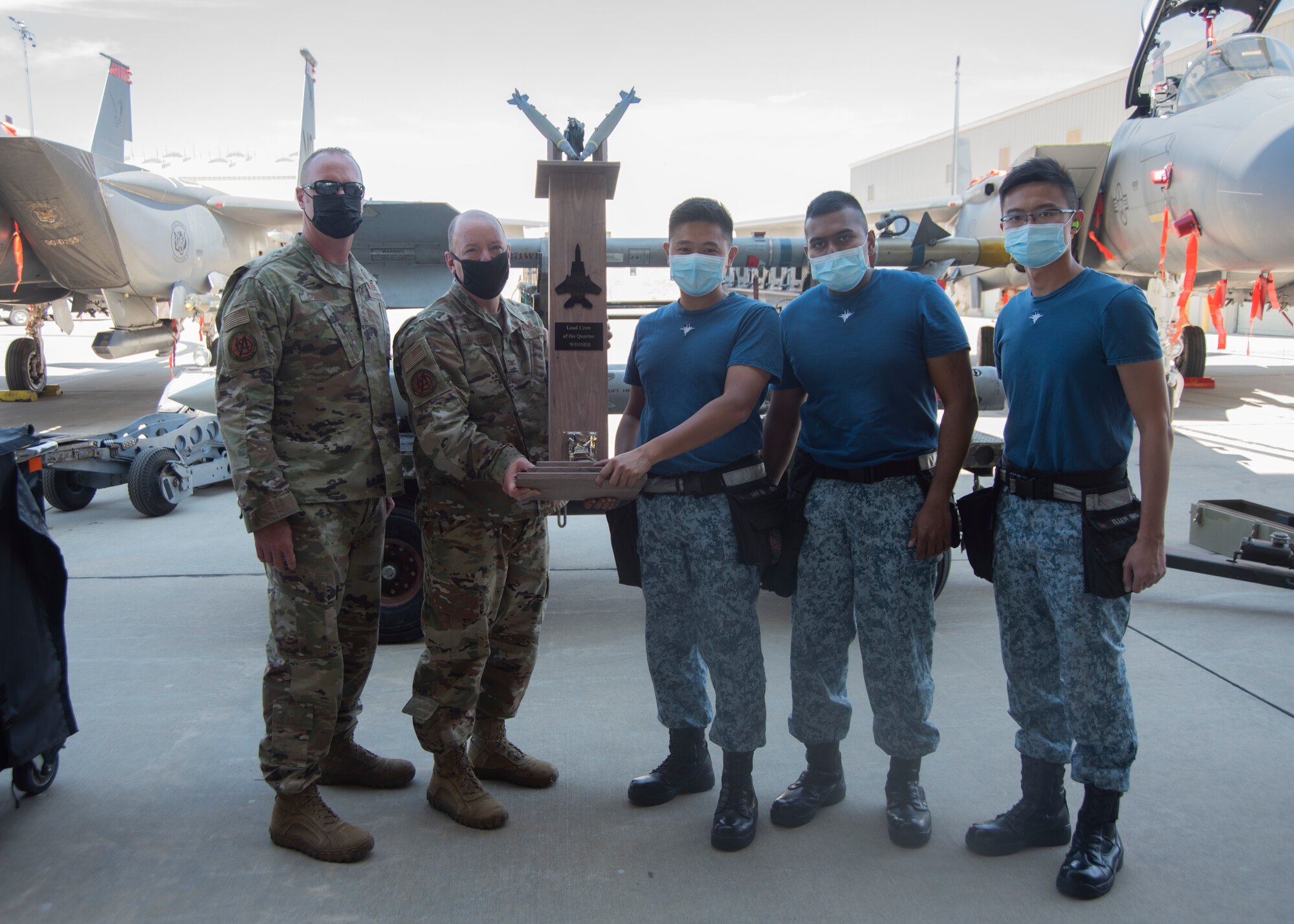 Two Airmen from the United States Air Force and Three Airmen from Republic of Singapore Air Force pose for a photo with the Quarterly Load Crew Competition trophy.