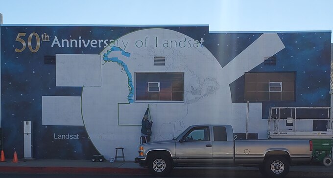 Ann Thompson, City of Lompoc Mural Society curator, sketches the Landsat satellite mural located on Ocean Avenue and I street on June 22, 2021, in Lompoc, California. Thompson was chosen to paint the mural by NASA to celebrate the 50th anniversary of Landsat. (U.S. Space Force photo by Airman First Class Tiarra Sibley)