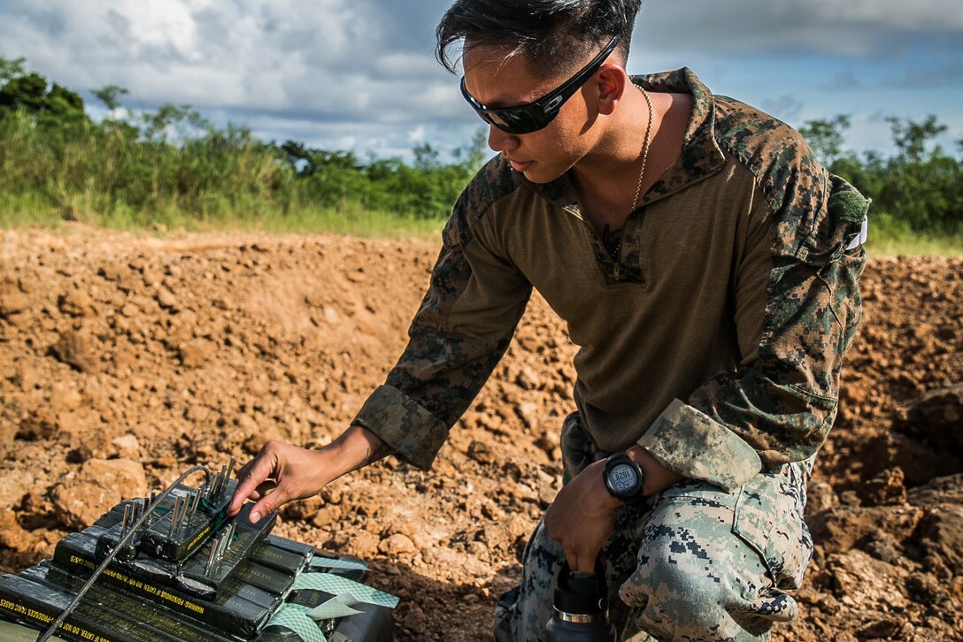 A Marine adjusts the controls on a device while crouched in a crater in a field.