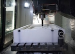 The Computer Numeric Control Machine is making cuts and trims on a large block of plastic.