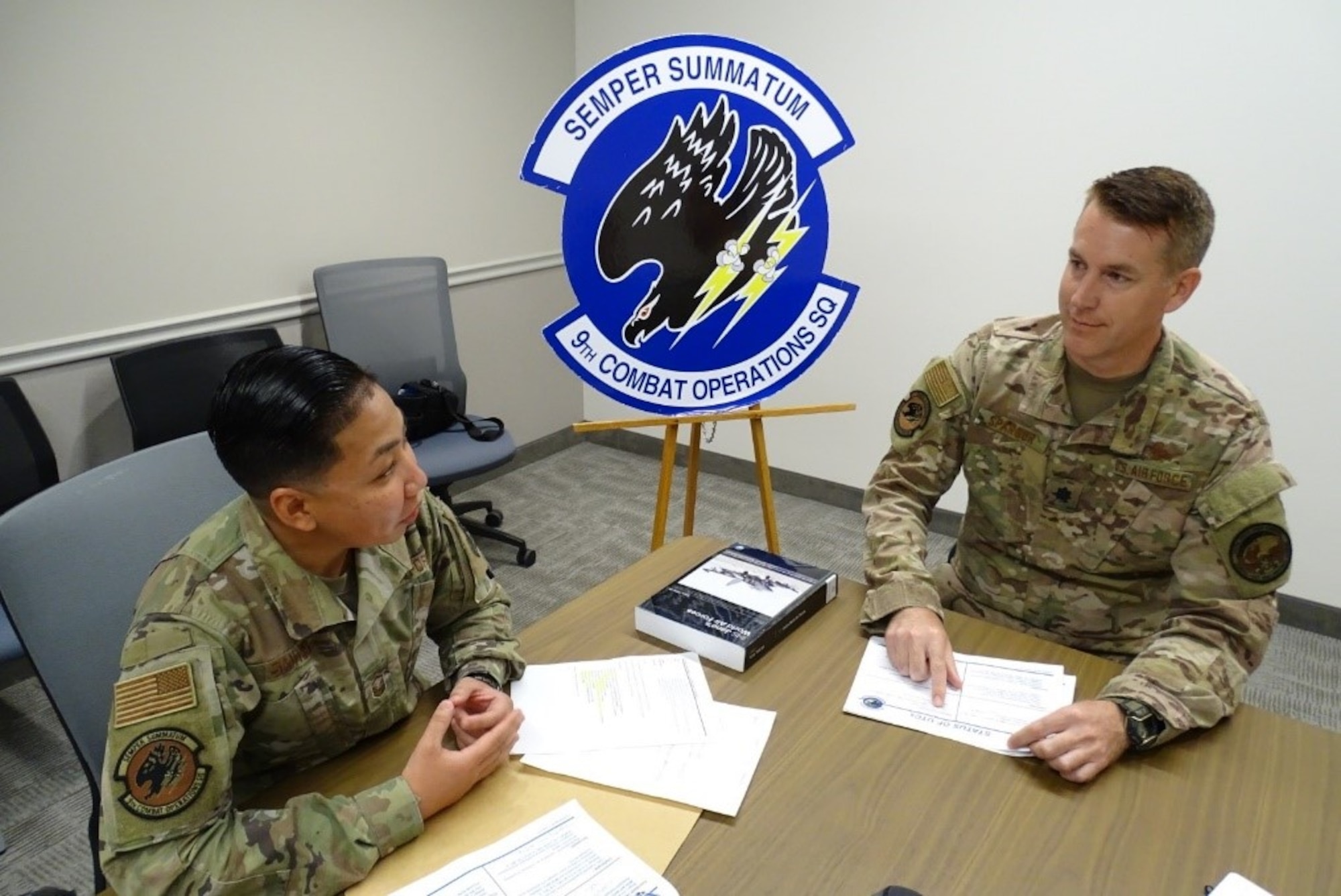 A man and a woman speaking while sitting at a table with papers in front of them.