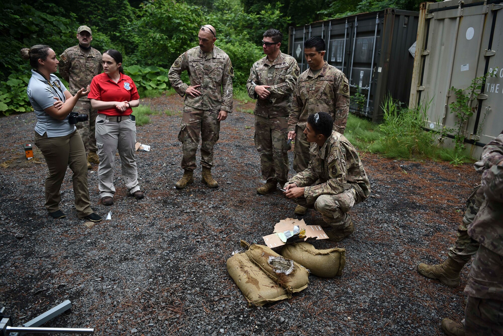Military members stand around a prop bomb made of cardboard that's bee shot with an anti-bomb device.