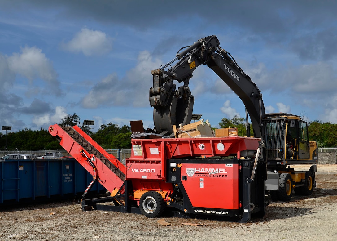 A small boom arm with a grapple attachment places used equipment into a  shredder.