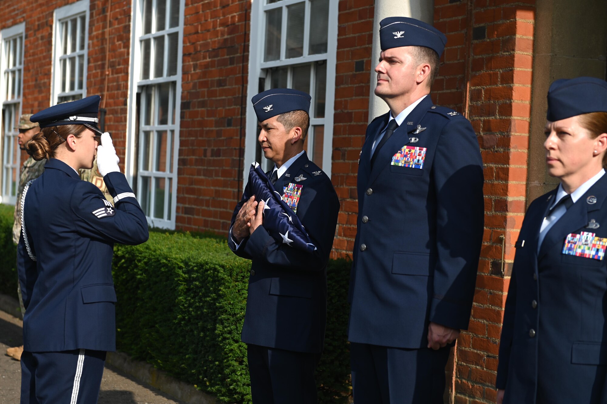 A member of the base honor guard team salutes U.S. Air Force Col. Troy Pananon, 100th Air Refueling Wing commander, after presenting him with a flag at Royal Air Force Mildenhall, England, July 19, 2021. The flag was given to Pananon to signify his last day of command as the 100th ARW commander. (U.S. Air Force photo by Staff Sgt. Matthew J. Wisher)
