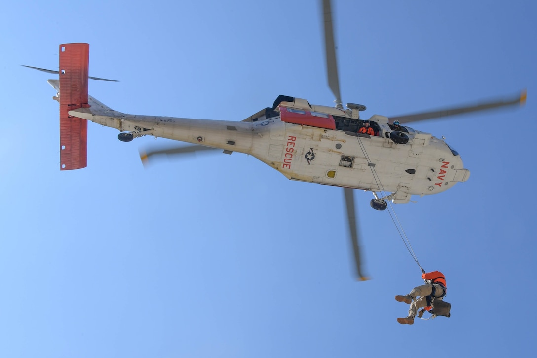 A sailor hangs on to a wire cord as he rappels down from a helicopter.
