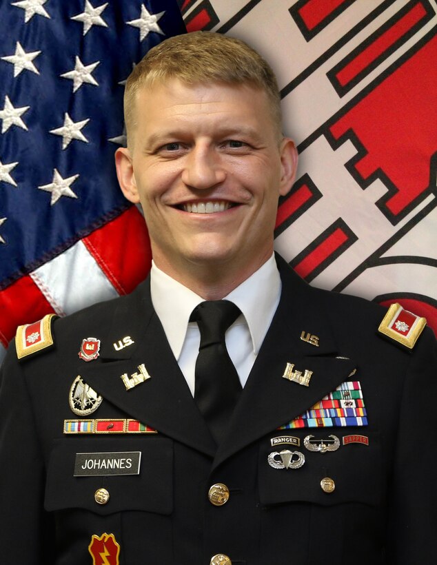 Man smiling in suit with flags behind him