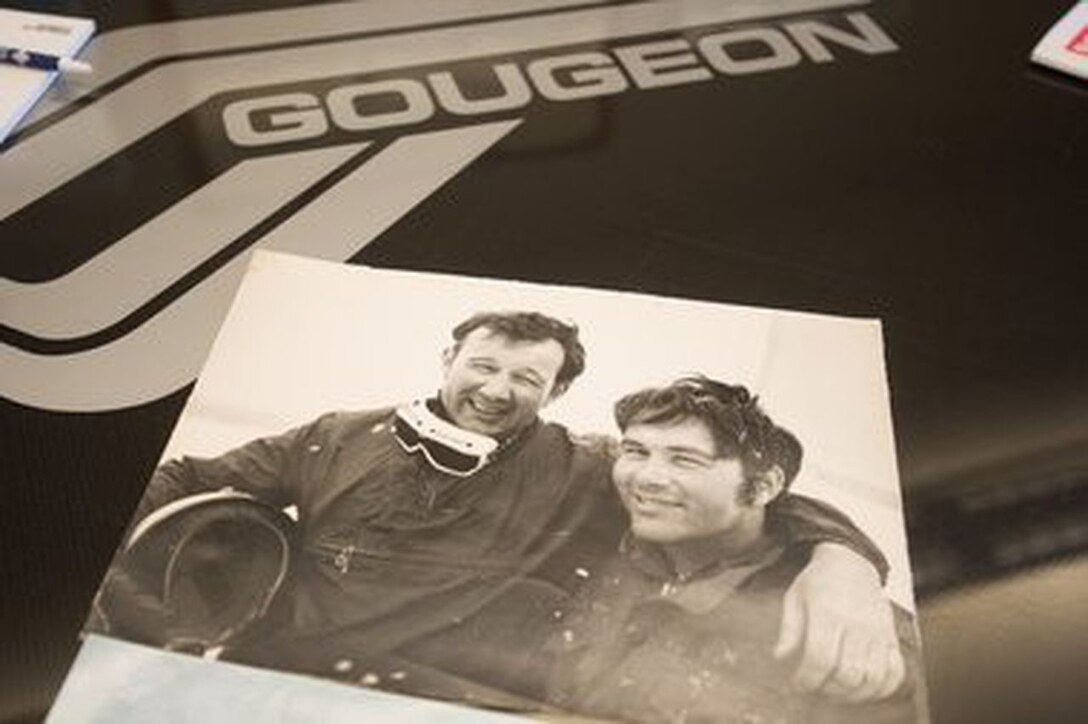 A photo that lays on a tabletop shows two men posing, one with his arm around the neck of the other.