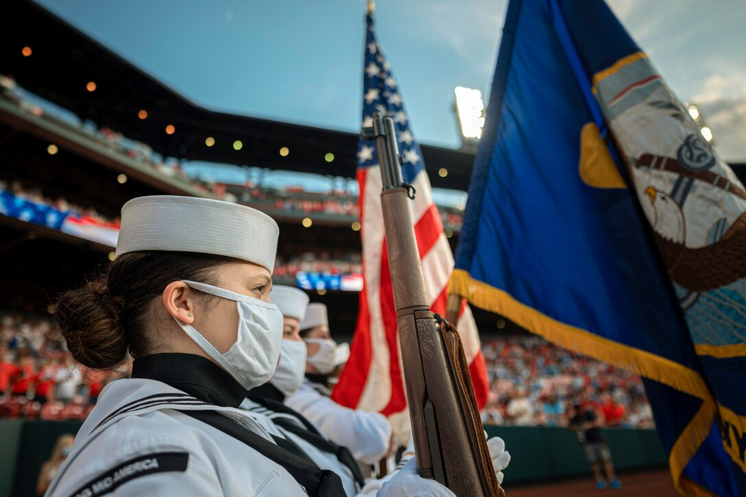 Members of the color guard present arms on a baseball field while fans watch.