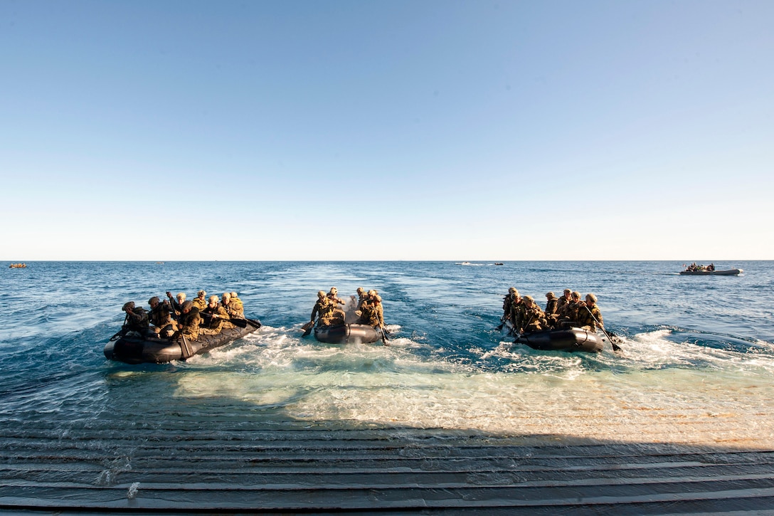 Marines ride in small boats behind a ship at sea.