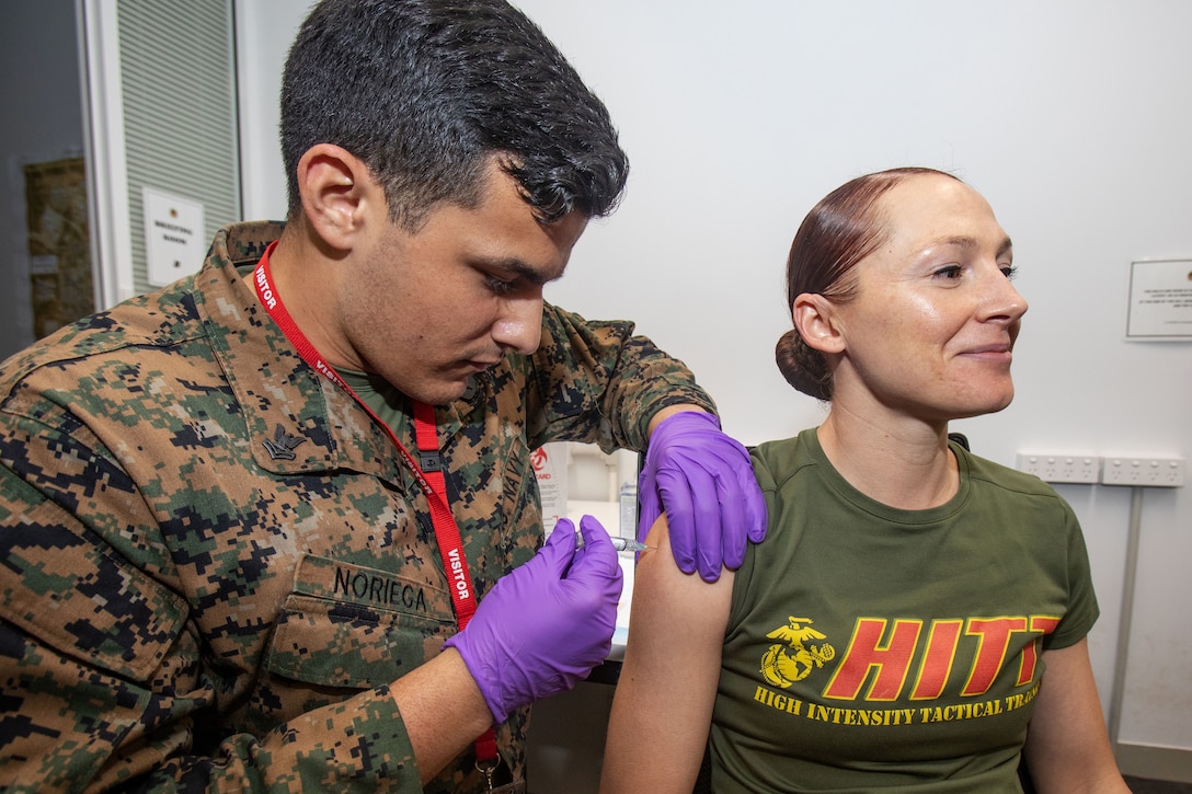 A soldier wearing gloves administers a vaccine to a Marine.