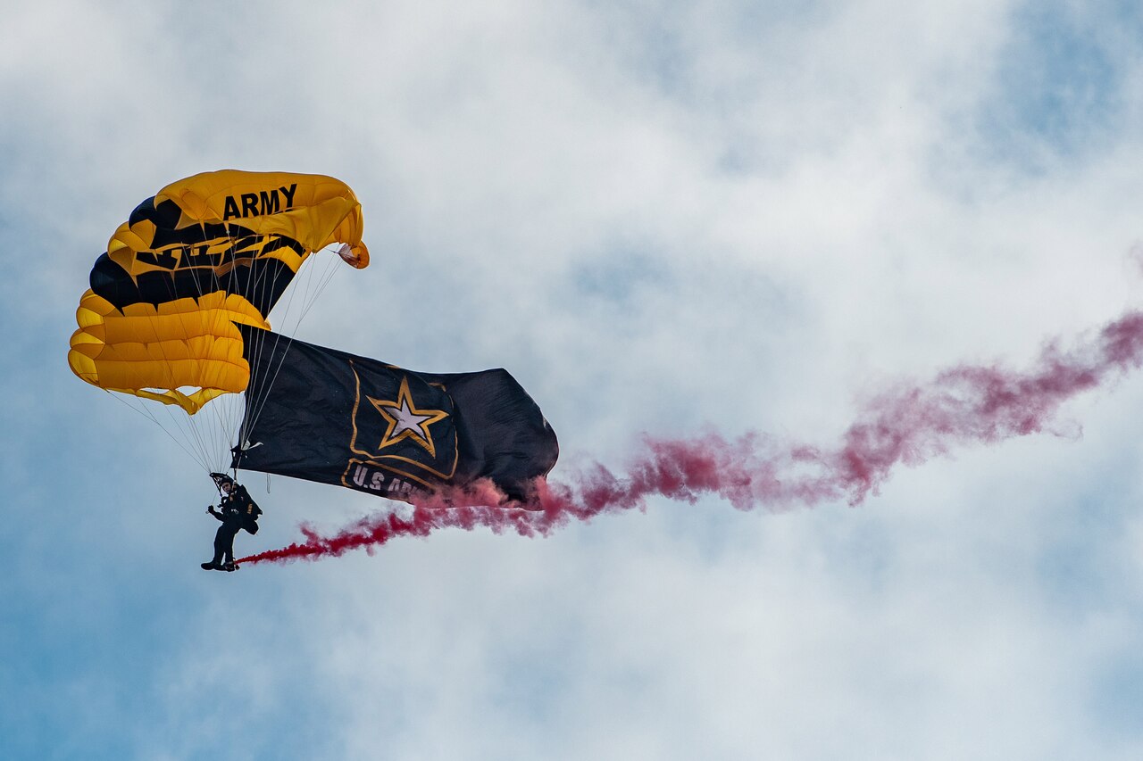 A Golden Knight prepares to land near a cloud of red smoke.