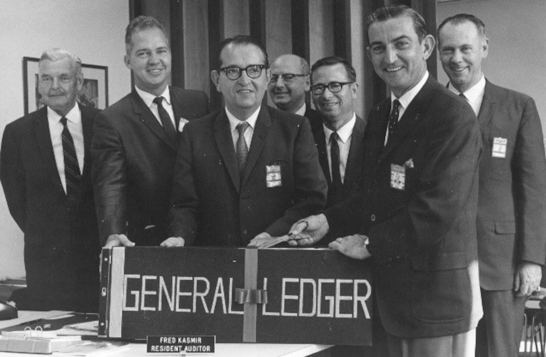 seven men in suits with a contractor's general ledger