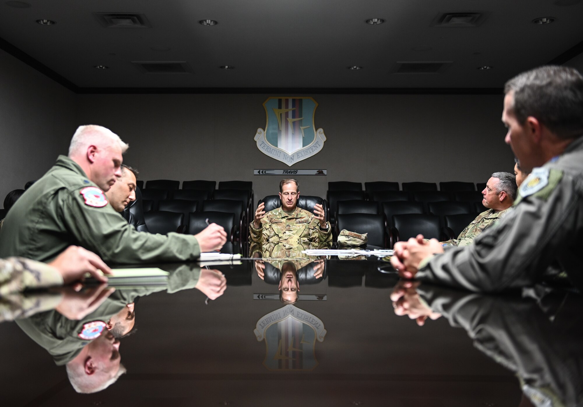 A man in a military uniform speaks to others inside of a dimly-lit conference room