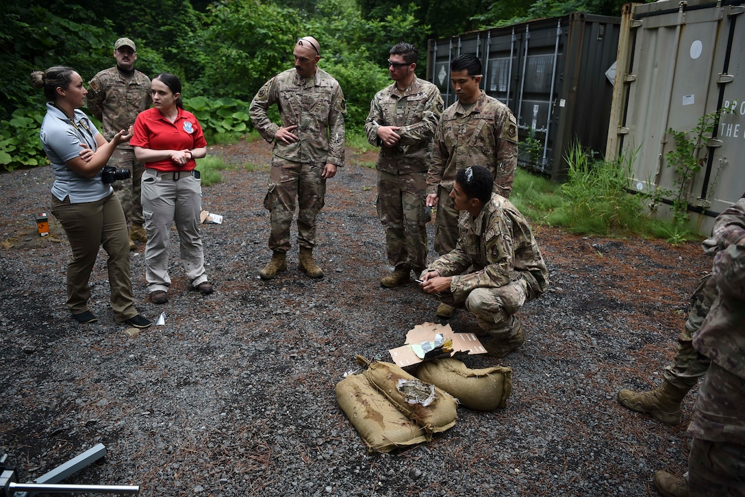 Military members stand around a prop bomb made of cardboard that's bee shot with an anti-bomb device.