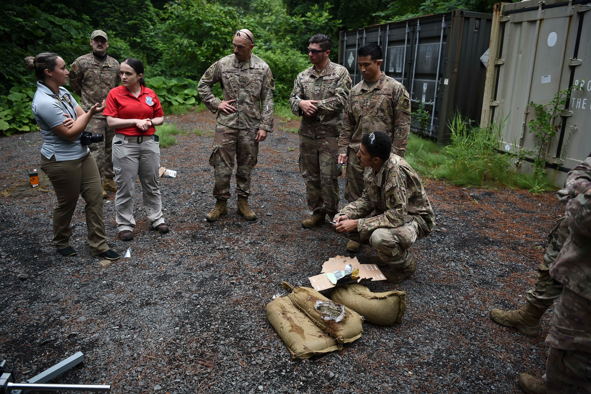 Military members stand around a prop bomb made of cardboard that's bee shot with an anti-bomb device.