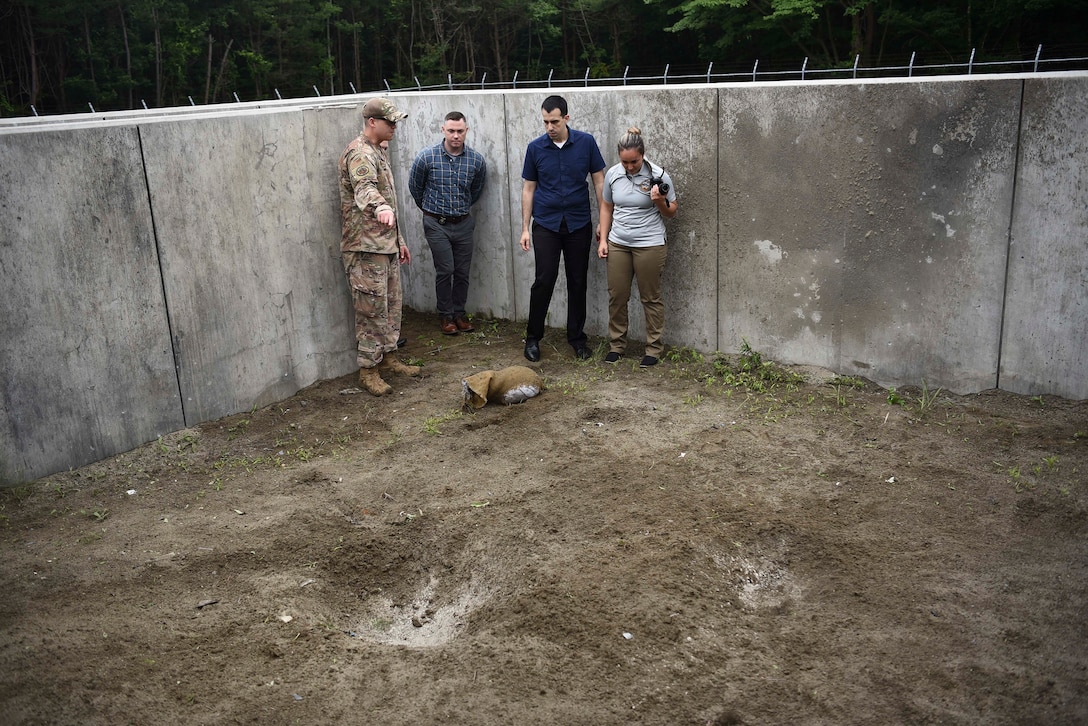 A military member points to a hole in the floor due to a controlled C-4 explosion.