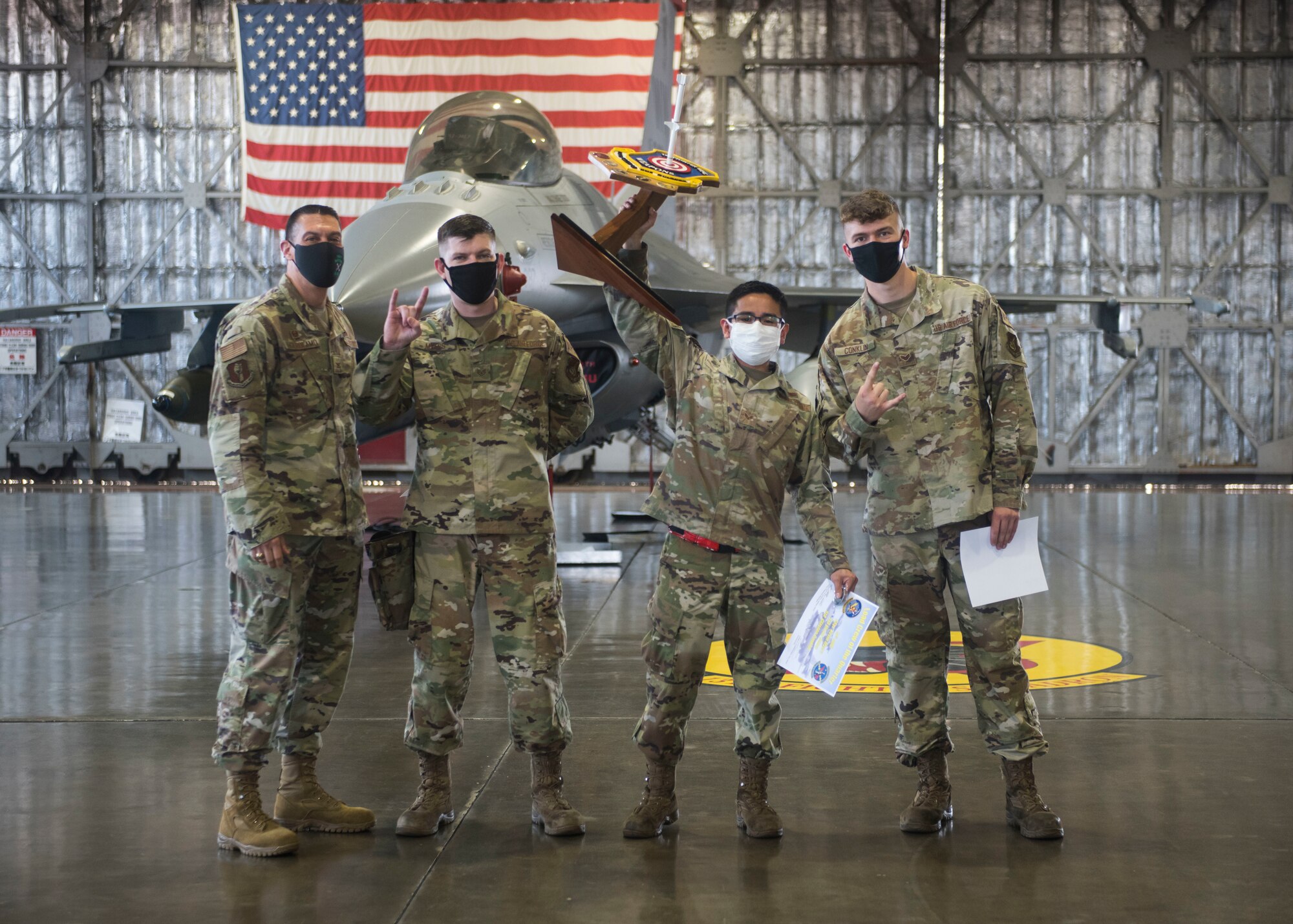 Group of military members hold a trophy in front of an F-16.