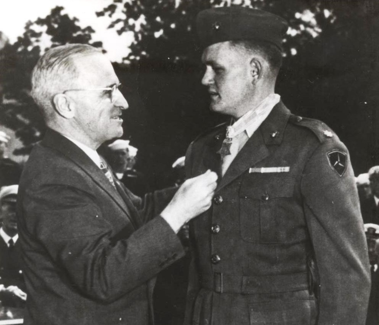 A man adjusts the lapel of another man's uniform.