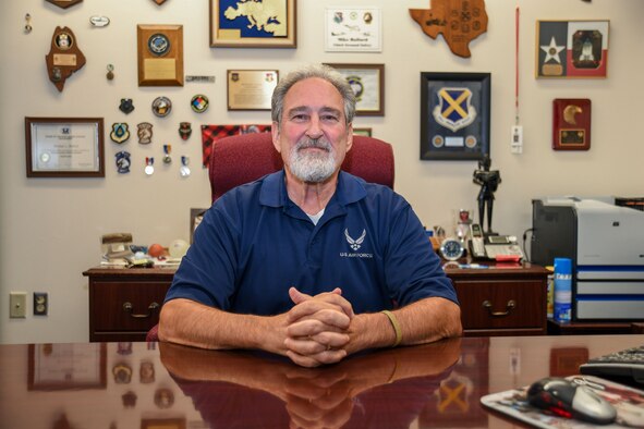 Ballard retires with more than 45 years of service. Photo of Ballard sitting proudly at his desk surrounded by many of his mementos from his years of safeguarding Airmen and Guardians.