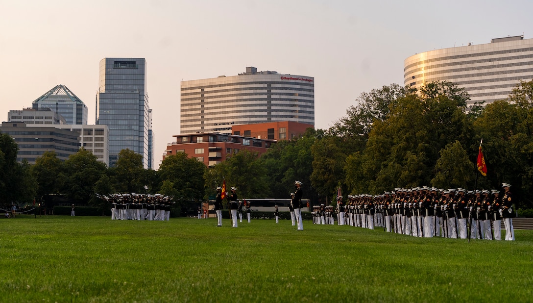 Marines of Company A, and Company B stand at ceremonial at ease as the Marines of the U.S. Marine Corps Silent Drill Platoon conduct a “Bursting Bomb” during a Tuesday Sunset Parade at the Marine Corps War Memorial, Arlington, VA, June 15 2021. The guest of honor for the evening was Ms. Kimberly Jackson, Deputy Assistant Secretary of Defense for Force Readiness, and Brig. Gen. Peter D. Huntley, Director, Operations Division, Plans, Policies and Operations, was the hosting official. (U.S. Marine Corps photo by Sgt. Jason Kolela)