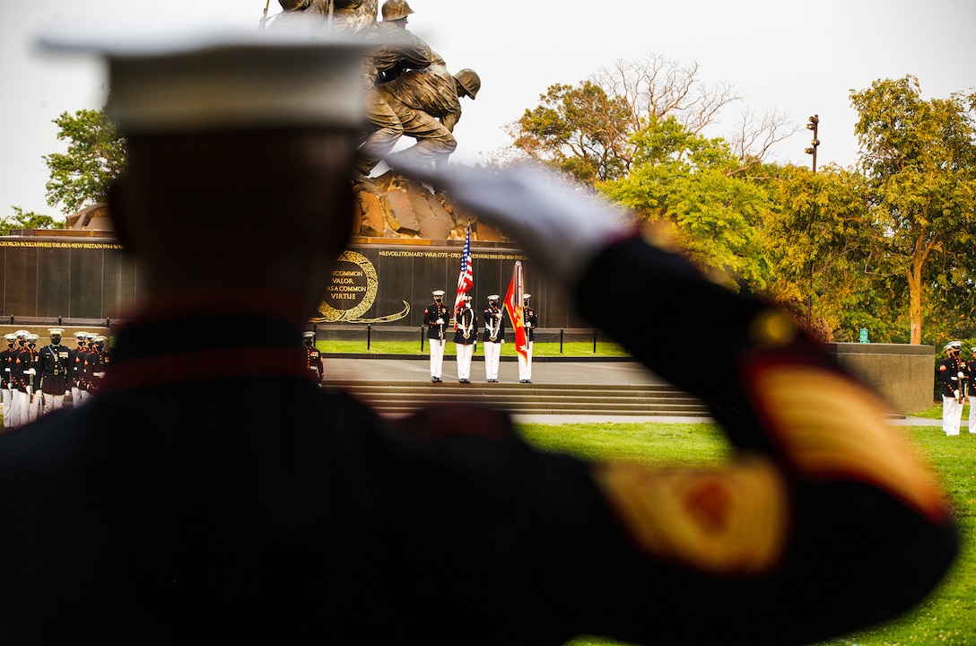 A Barracks Marine salutes as The Official U.S. Marine Corps Color Guard presents the National Ensign during a Tuesday Sunset Parade at the Marine Corps War Memorial, Arlington, VA, June 15 2021.