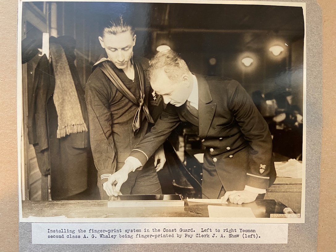 A photo of installing the finger-print system in the Coast Guard.  Left to right Yeoman second class A. G. Whaley being finger-printed by Pay Clerk J. A. Shaw.