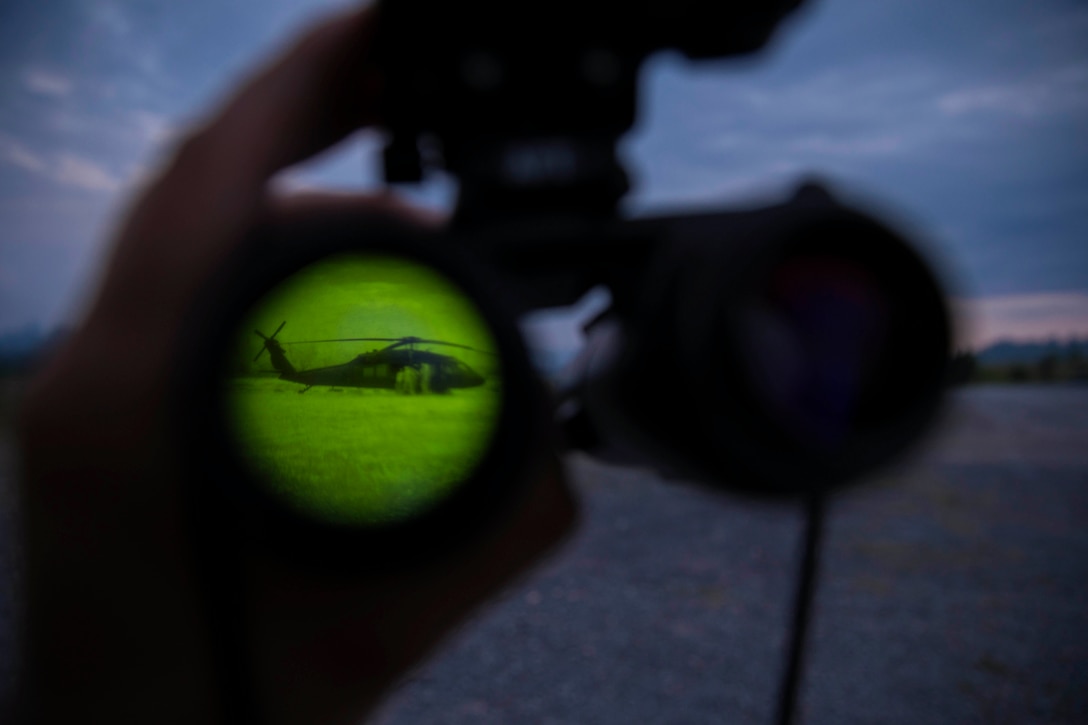 Soldiers load a helicopter as seen through night vision binoculars.