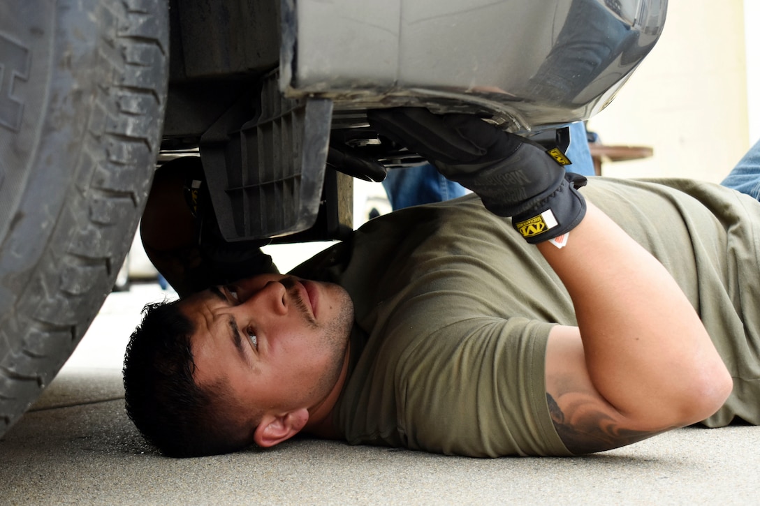 A soldier lays on his back and searches under a vehicle.