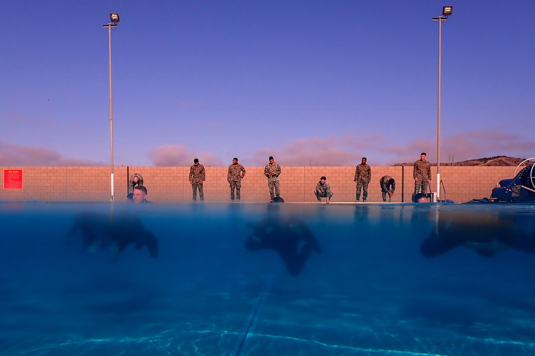 Marines swim across a pool while fellow Marines observe.
