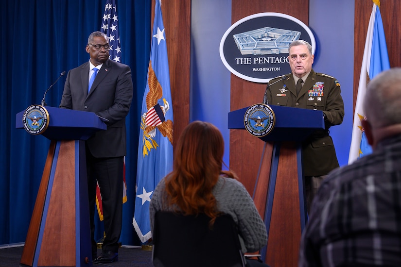 Defense secretary and Joint Chiefs chairman stand at lecterns in front of a seated audience.
