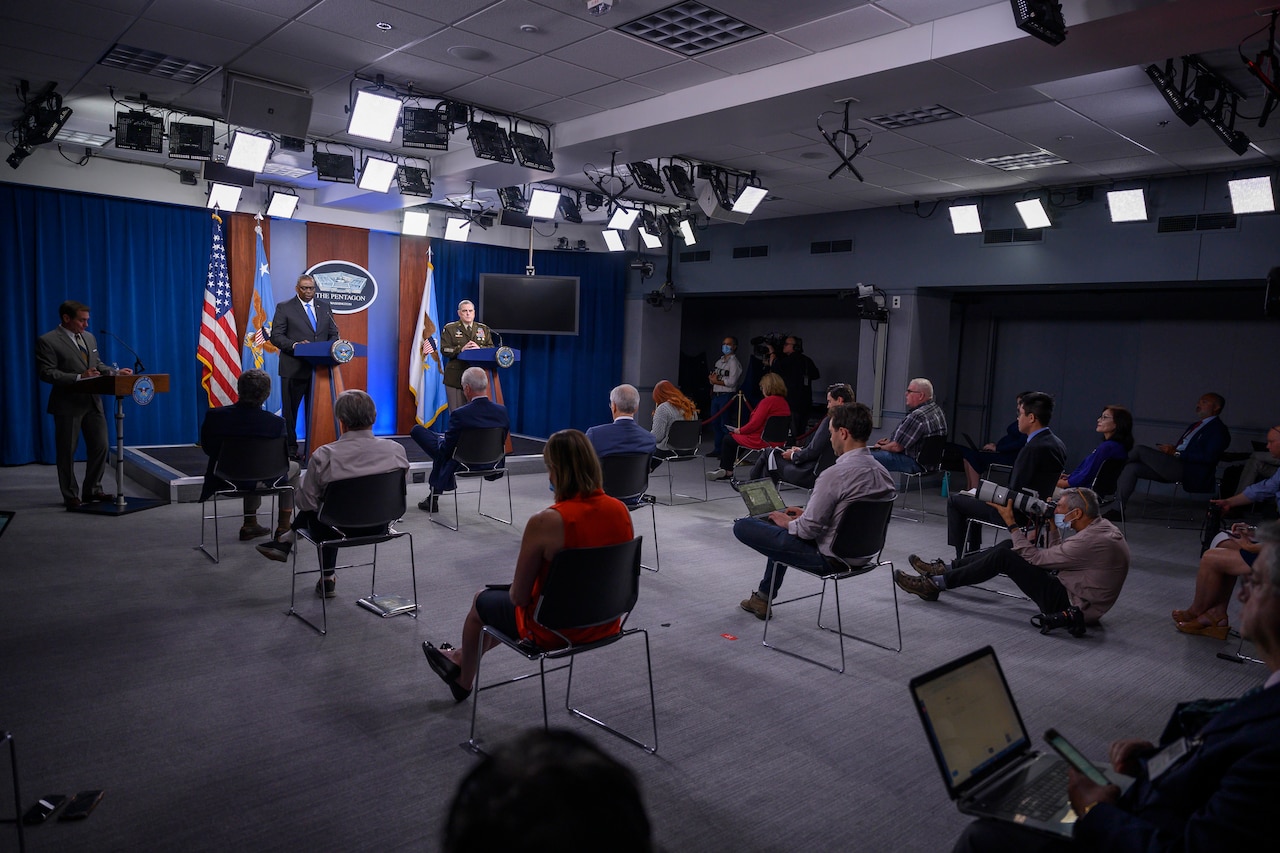 Defense secretary and Joint Chiefs chairman stand at lecterns in front of a seated audience.