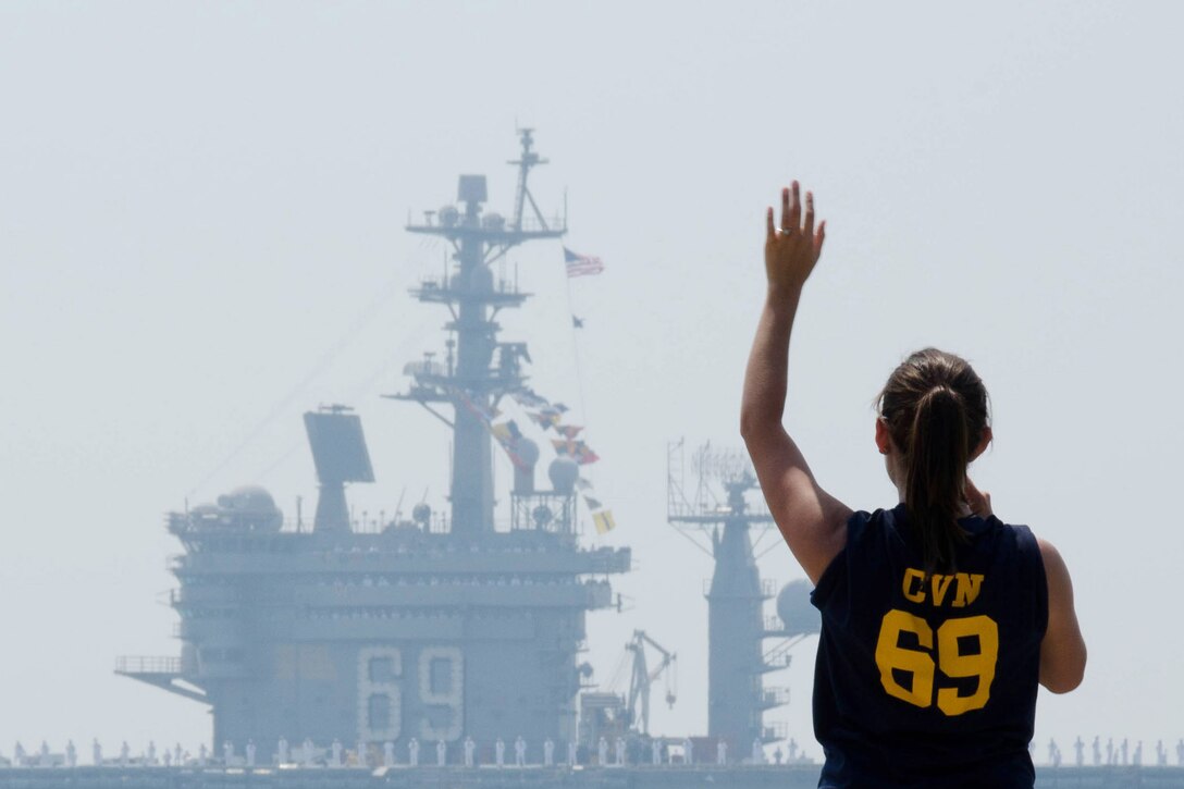 A woman waves as a ship passes in the distance.