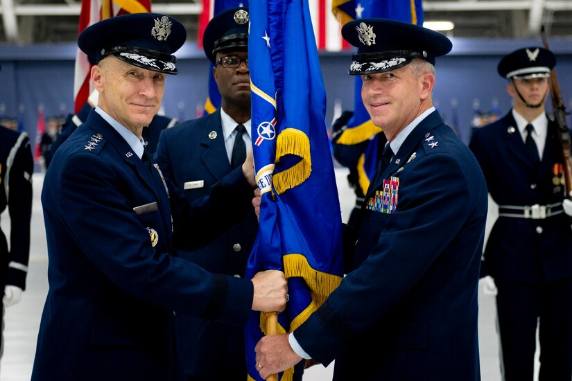 Two men look at camera as guidon is passed.