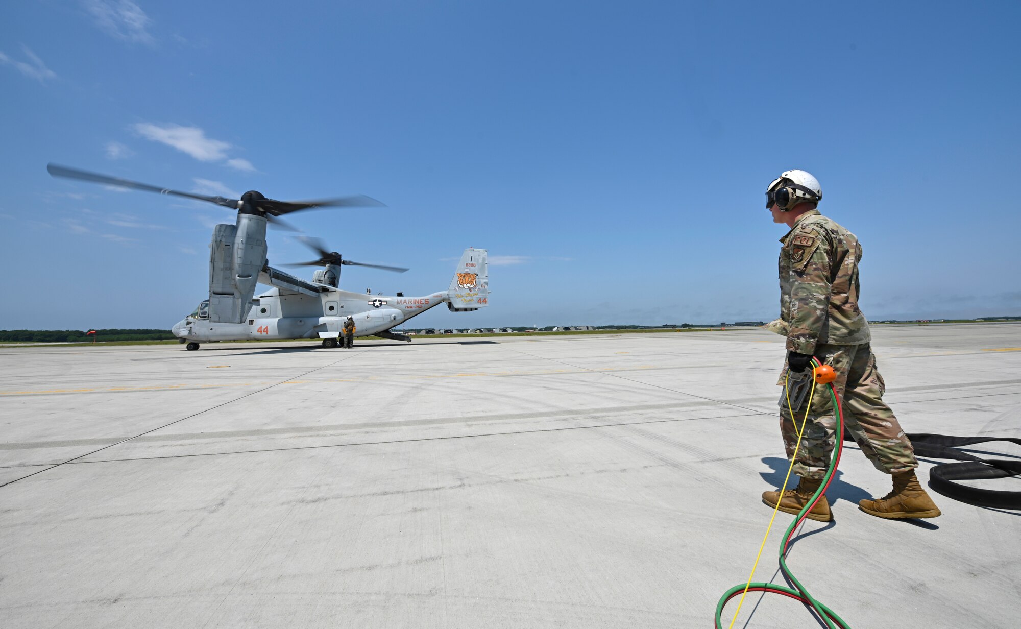 An Airman stands with cables in his hand looking at a tiltrotor aircraft.