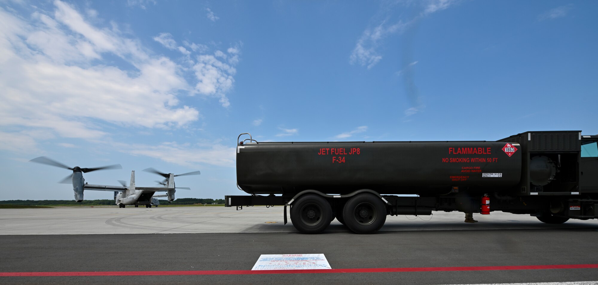 A tiltrotor aircraft and a fuel truck are parked on a flight line.