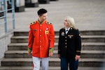 ROK Army Sgt. Yook Sung-jae in dress uniform is standing on the left while U.S. Army Spc. Brittany D. Simmons in dress uniform is standing on the right and both are looking at one another, talking. Behind them is a blurred stairway from inside of the War Memorial of Korea.