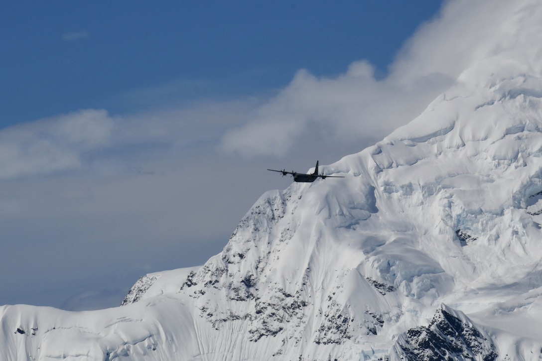 A military aircraft flies near a snowy mountain.