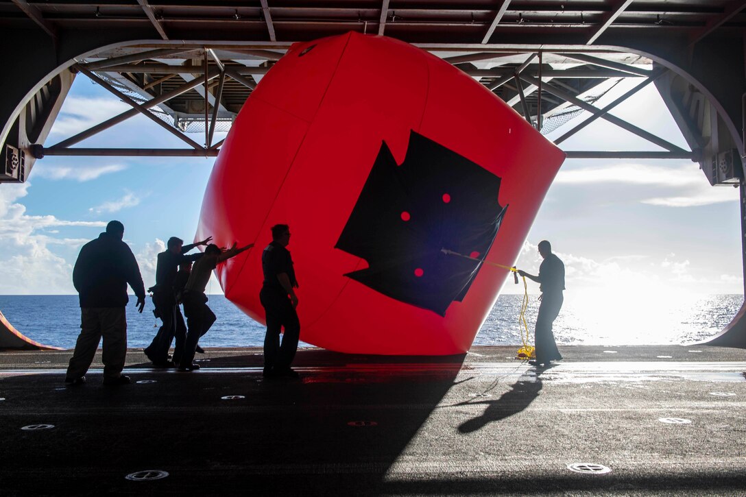 Sailors set up a large red inflatable target on a ship.