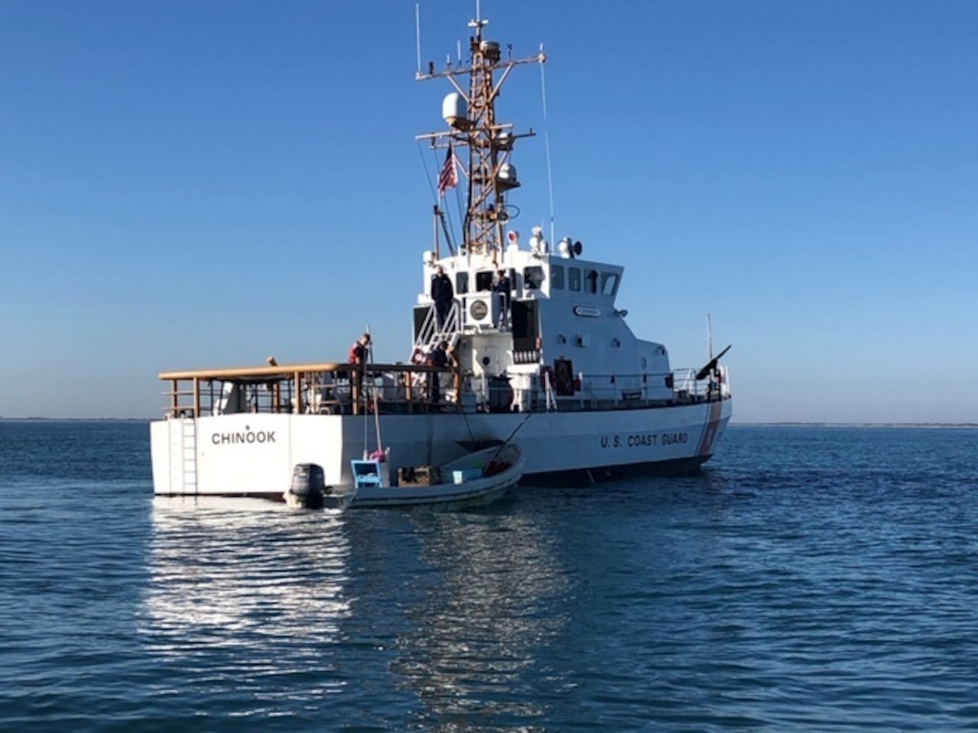 A Coast Guard vessel floats beside a small boat.