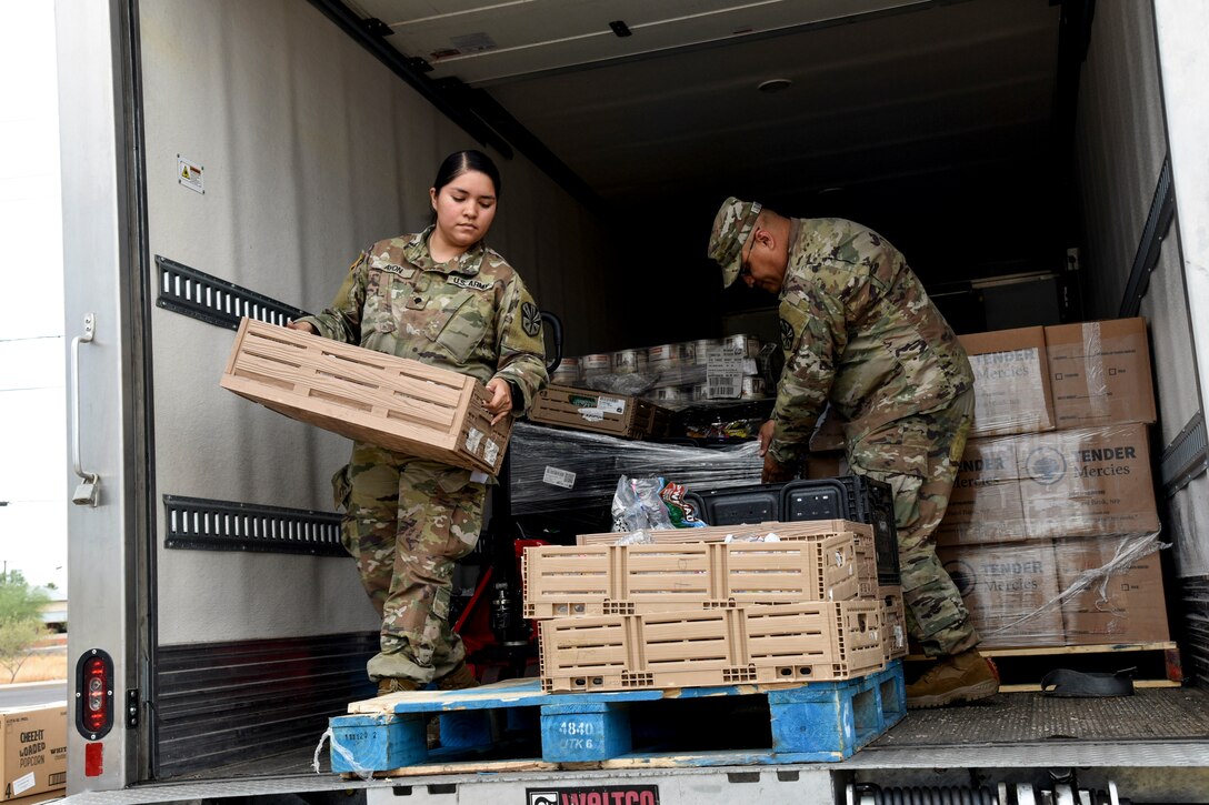 Two soldiers handle containers in the back of a cargo truck.