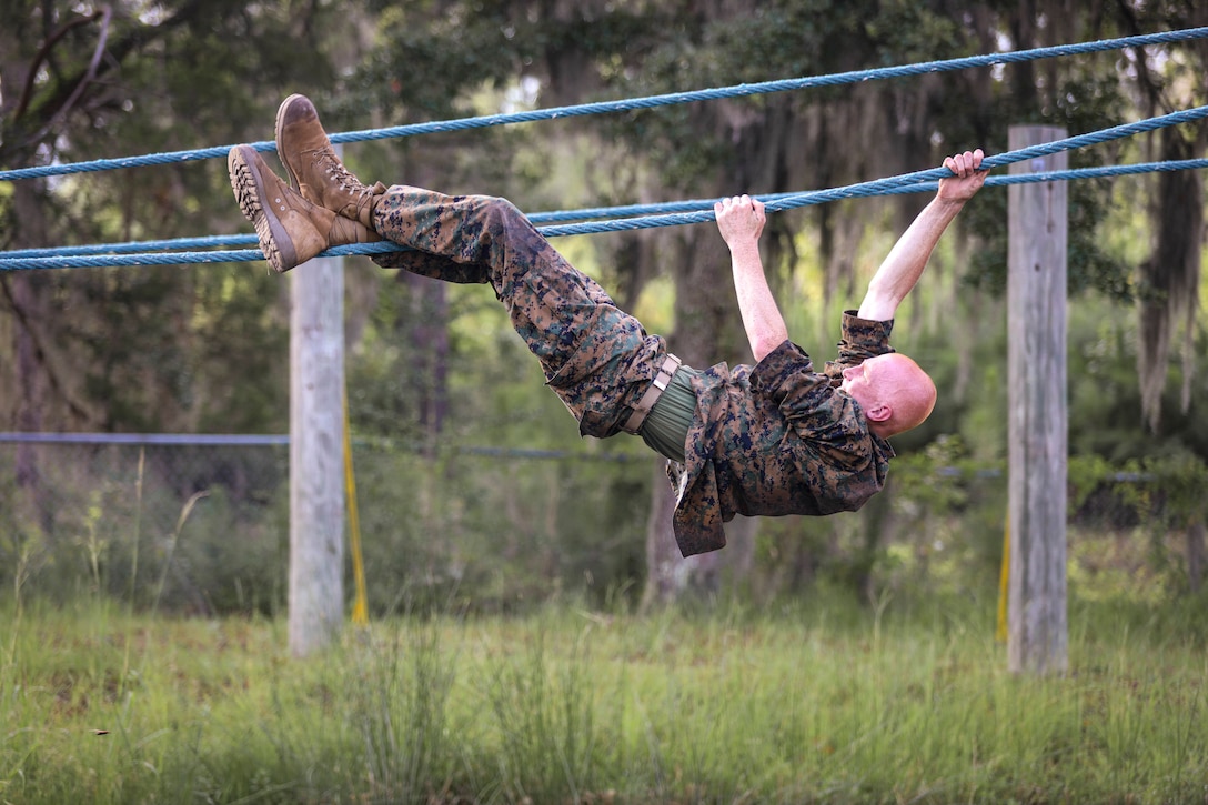 A Marine Corps recruit climbs inverted across a rope.