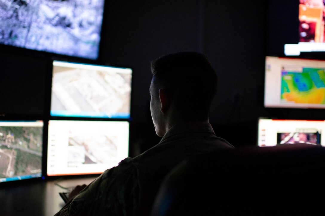 Individuals sit in a darkened room lit only by computer screens.